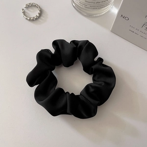 Detailed view of a soft black satin scrunchie with elegant silk gloss on white background