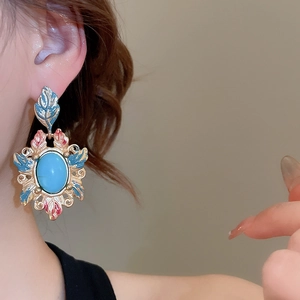 Close-up of vintage gold earring with blue oval gemstone and enamel floral details