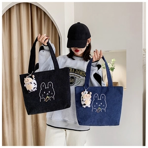 Detail of corduroy tote bags in black and navy with rabbit embroidery and cow plush charms