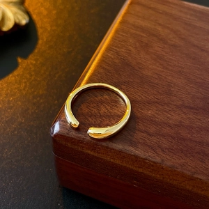 Detailed view of a gold-plated teardrop open ring on a dark wooden display surface