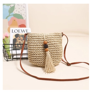 Detail of beige straw crossbody bag with wooden beads and tassels on a bright background