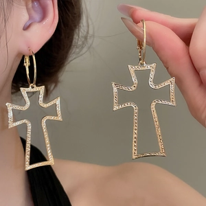 Detailed close-up of gold hollow cross hoop earrings featuring unique textured hammered finish