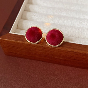 Macro view of round red velvet stud earrings with golden metallic outer frame