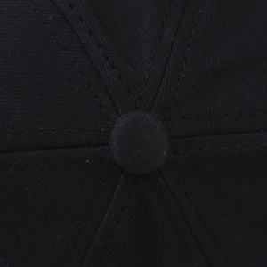 Macro detail of the crown seam and top button on a black washed cotton baseball cap