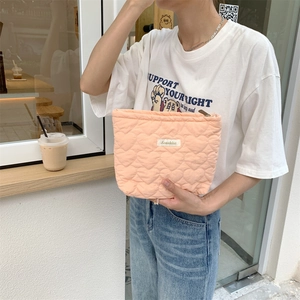 Close-up of quilted heart pattern vanity pouch in peach pink held by a model