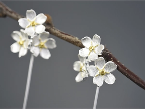 Macro shot of silver flower drop earrings with golden pistils on a wooden branch
