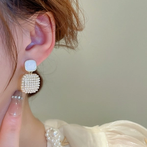 Elegant gold square pearl earrings with light blue gemstone detail on a female model