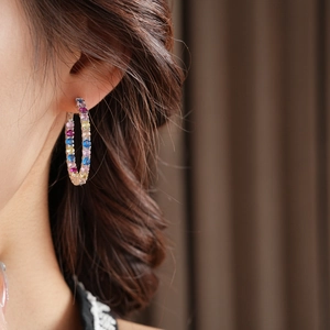 Primo piano di eleganti orecchini a cerchio in oro rosa con zirconi colorati sulla modella