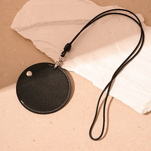 Detail of round black faux leather pendant with silver clasp and woven lanyard on stone surface