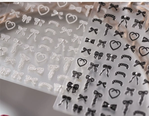 Macro detail of 3D bow and heart nail stickers with pearl accents on transparent backing