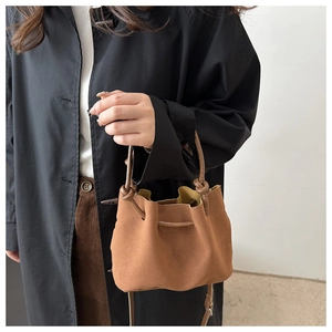 Close-up of brown suede bucket bag with drawstring closure held by a model