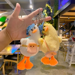 Plush duck keychains with hats and small bags shown in hand for size and texture detail