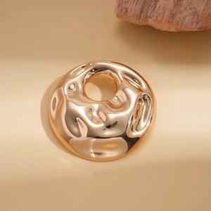 Close-up of gold-plated hollow circular brooch with hammered texture and organic design