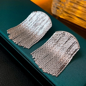 Macro detail of silver fan-shaped fringe earrings with tassels on green leather texture