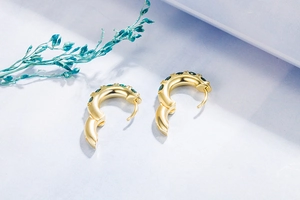 Detailed view of gold hoop earrings with emerald green crystals on purple background