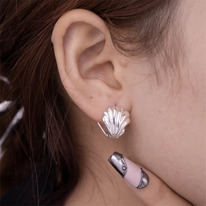 Macro side view of a polished silver shell-shaped crescent hoop earring worn by a model