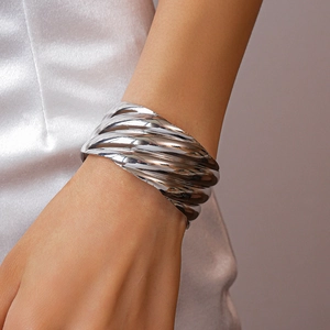 Close-up of a wide silver cuff bracelet with irregular wave texture on a model wrist