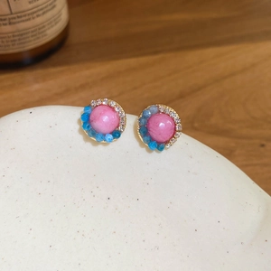 Detail view of pink crystal stud earrings with blue beads and zircon on stone