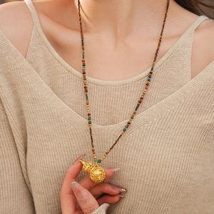 Macro shot of gold hollow gourd pendant necklace with colorful beads on a model