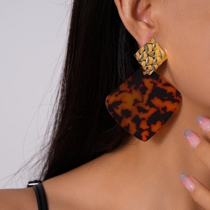 Close-up of geometric diamond-shaped tortoise shell acrylic earrings worn by a model