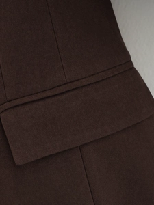 Macro detail of the pocket flap and fine twill fabric texture on a dark brown blazer
