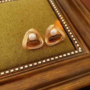 Detail of vintage triangular gold earrings with white pearl and amber stone on green fabric