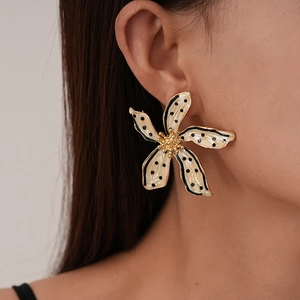 Détail de boucles d'oreilles fleurs crème avec pois noirs et centre doré sur modèle