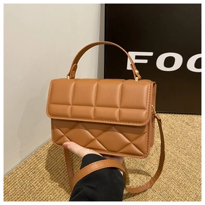 Detail of a brown quilted leather crossbody bag featuring hand grip and long strap