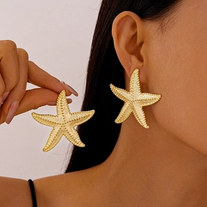 Detailed view of large gold starfish earrings with textured surface on a female model