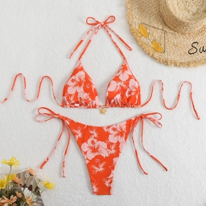 Detailed flat lay of orange floral bikini with gold flower pendant and beach accessories