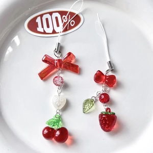 Handmade cherry and strawberry beaded charms with red resin bows on a white porcelain tray