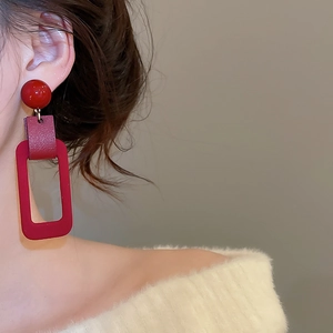 Detail view of red flocked geometric rectangular drop earrings on model with white sweater