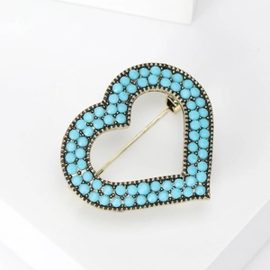 Detailed close-up of a heart-shaped bronze brooch with blue beads on white background