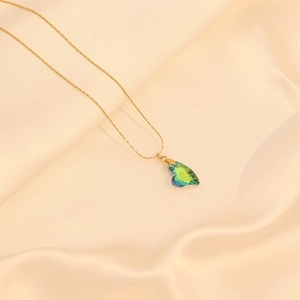 Détail d'un pendentif cœur en cristal vert sur une chaîne vénitienne dorée et soie