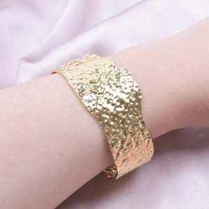Close-up of golden wide cuff bracelet with hammered texture and wavy edges on silk