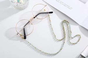 Detail of light blue crystal bead eyewear chain with gold frame glasses on white background