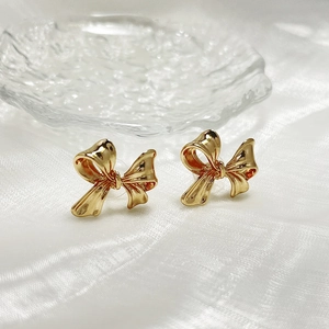 Macro view of gold bow knot earrings with high-polish finish on a textured silk background