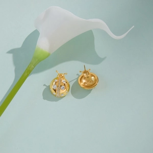 Vue détaillée de boucles d'oreilles coccinelle dorées avec strass blancs sur fond bleu