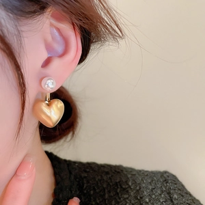 Close-up detail of heart pearl earrings showing matte gold texture and shiny pearl