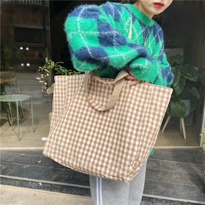 Detail of a large checkered canvas tote bag with brown woven handles in a street setting
