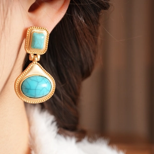 Close-up of vintage gold teardrop earrings featuring turquoise resin stones on a model