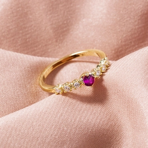 Macro shot of gold-plated ring with ruby-colored stone on smooth pink silk fabric