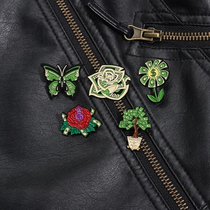 Detail of five creative enamel pins with money and floral designs on a black leather jacket