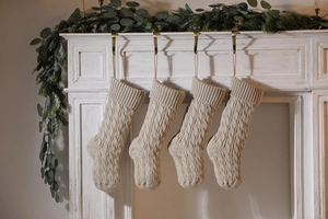 Detail of four beige cable knit Christmas stockings hanging on a white festive mantel