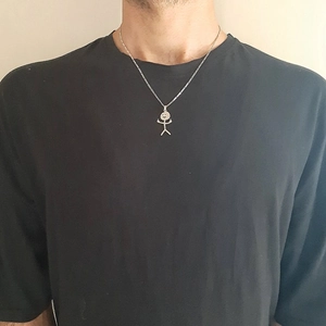 Close-up of funny silver middle finger stickman doodle necklace worn by a person