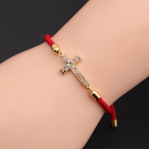 Wrist-worn view of gold-plated cross bracelet with colorful cubic zirconia and red cord