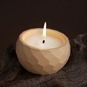 Modern geometric faceted candle jar with textured surface and warm glowing candlelight
