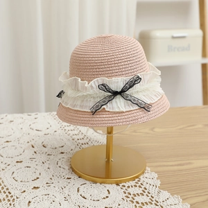 Détail d'un chapeau de paille rose avec dentelle blanche et nœud noir sur support
