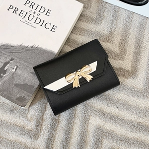 Short black leather wallet for women with golden bow and contrast strap on fur background