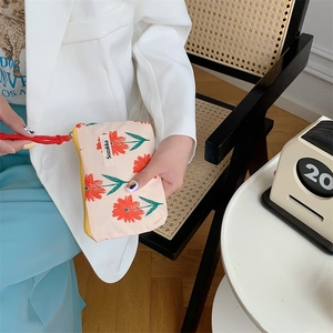 Detail of floral makeup bag with red drawstring, showing beige fabric and leaf patterns